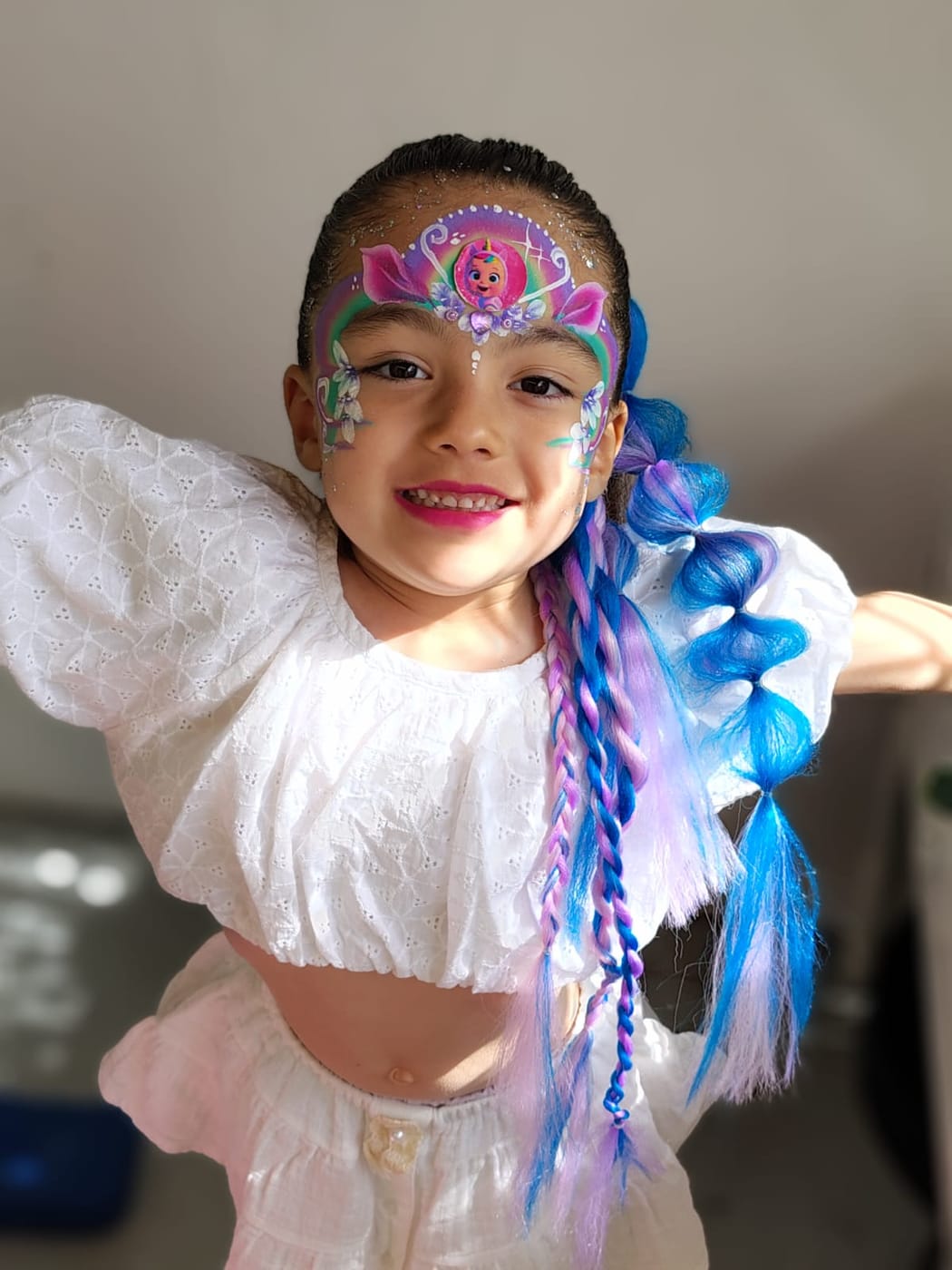 Nena sonriendo con una corona pintada en violeta y rosa y coletas de colores